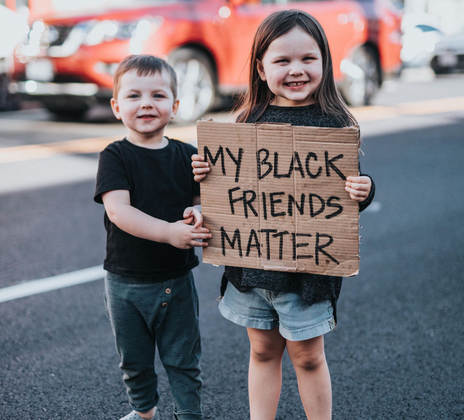 Kitchen Table CEOs Blog - How to Celebrate Black History with your Family year round - 2 children smiling at camera with a cardboard sign that says My Black Friends Matter
